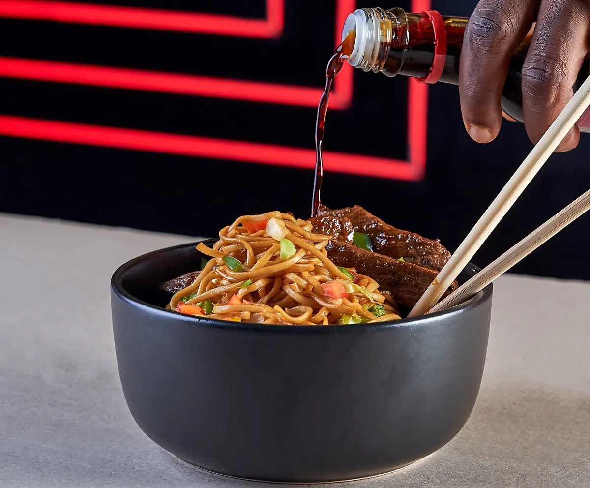 Lo mein noodles with steak, soy sauce being poured
